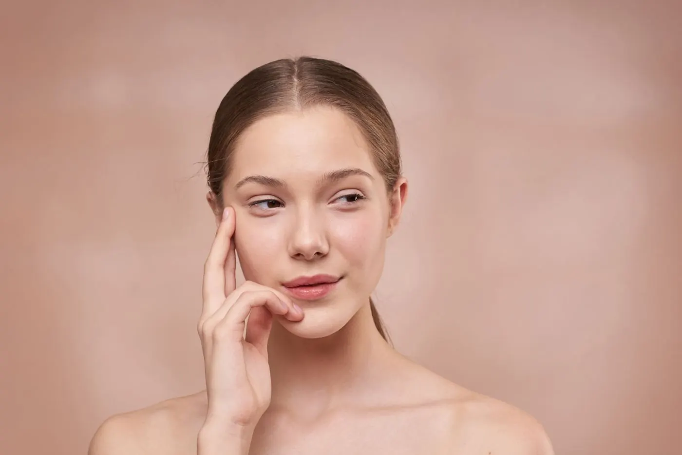 Cô gái chạm nhẹ tay lên thái dương trên nền hồng be